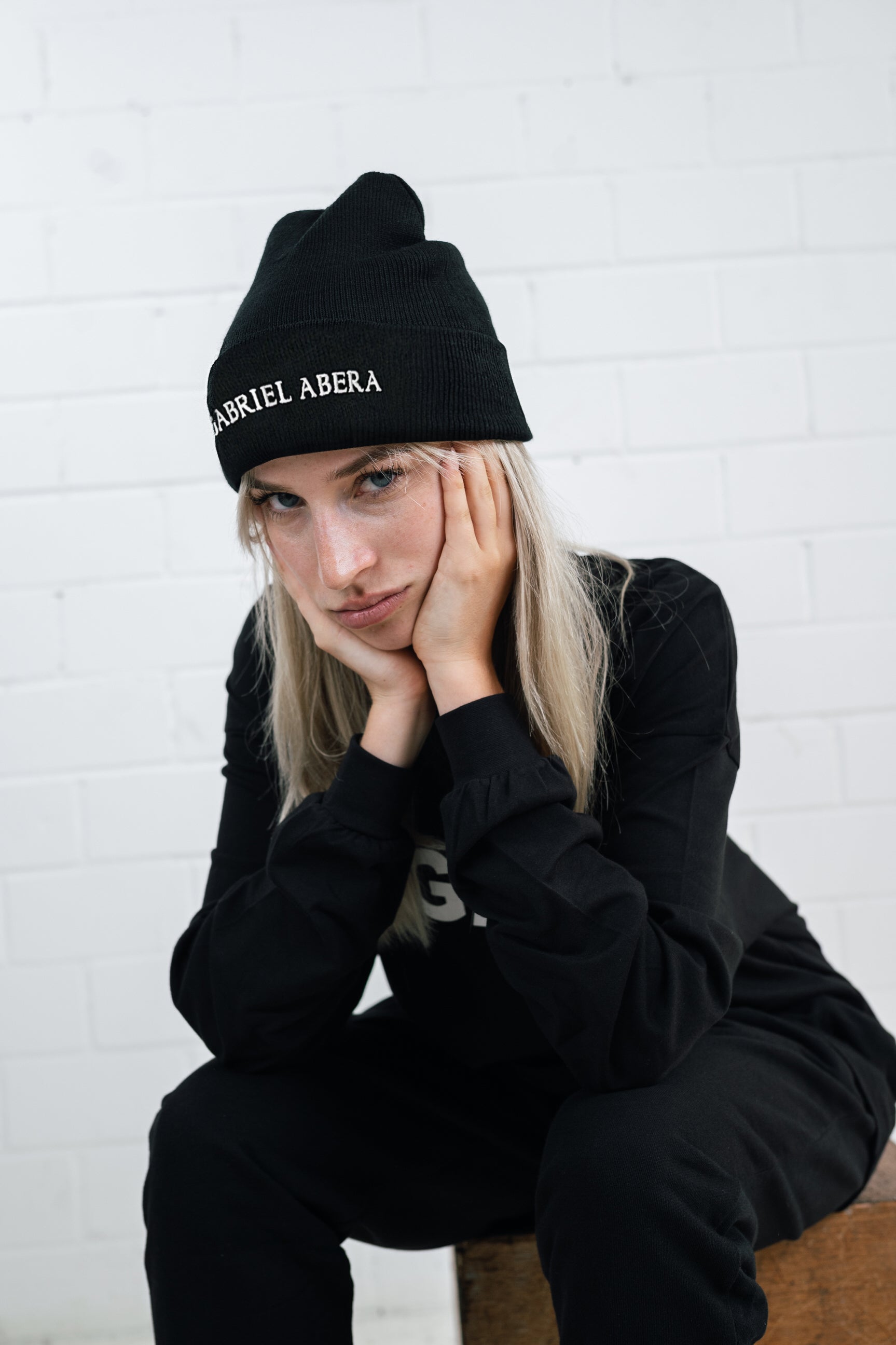 Female model wearing a Black beanie with brand name embroidery